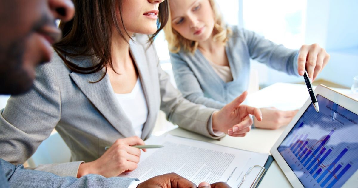 Three business valuation appraisers reviewing a chart on a tablet computer showing revenue growth statistics